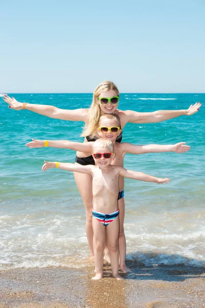 Moeder en twee zonen in zonnebril rusten en spelen op het strand... Zomer familie vakantie. — Stockfoto