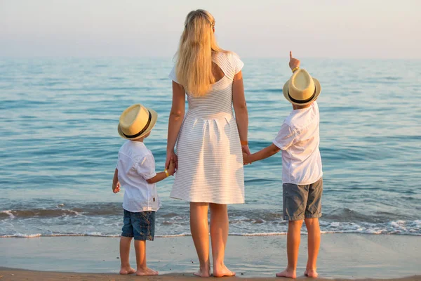 Familie wandelen op het strand 's avonds tijdens zonsondergang. Moeder en twee zonen. — Stockfoto