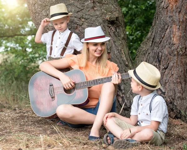 Młoda matka i dwóch synów spoczywają w lesie, śpiewanie piosenek z gitarą. — Zdjęcie stockowe