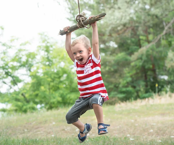 Pequeño niño montando en un columpio improvisado en el bosque . — Foto de Stock