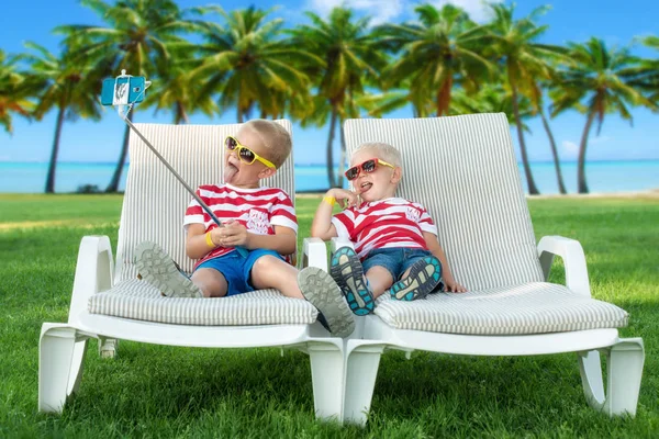 Two brothers lying on the sun loungers and take selfie on mobile phone.Hot summer holidays. — Stock Photo, Image