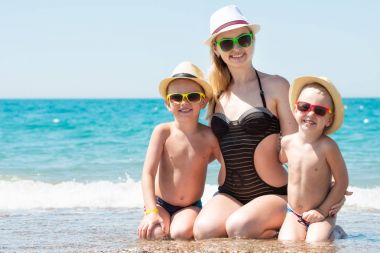 Anne ve iki oğlu şapka sahilde oturuyor. Aile tatil yaz.