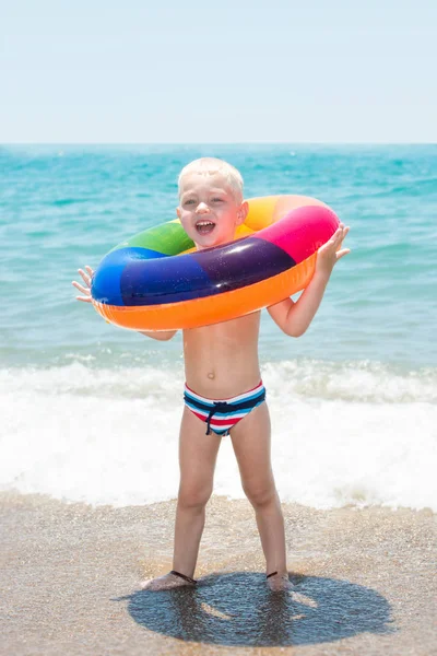 Niño feliz jugando con el anillo inflable colorido en día caliente del verano. Juguetes de agua infantil. Los niños juegan en el resort tropical. Vacaciones familiares en playa — Foto de Stock