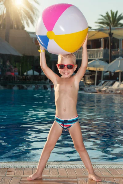 A little boy plays with an inflatable ball in the pool.Water toy and sunglasses for kids. — Stock Photo, Image