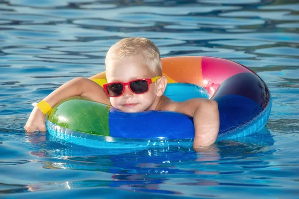 Feliz niño jugando con el anillo inflable colorido en la piscina al aire libre en el día caliente del verano. Los niños aprenden a nadar. Juguetes de agua infantil. Los niños juegan en el resort tropical. Vacaciones familiares en playa — Foto de Stock