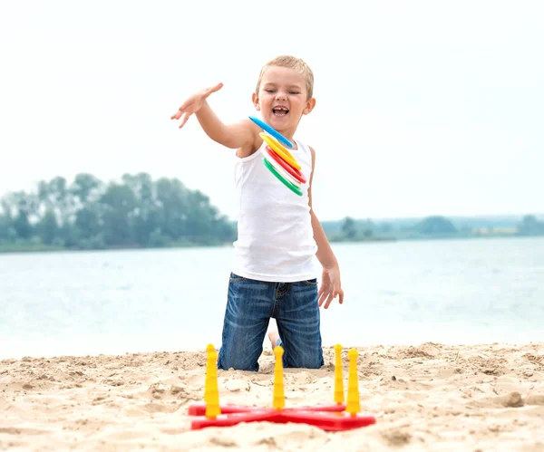 Cute boy playing a game throwing rings on the seafront.The joy of victory. — Stock Photo, Image