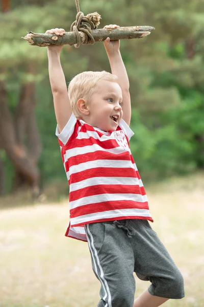 Pequeño niño montando en un columpio improvisado en el bosque . — Foto de Stock