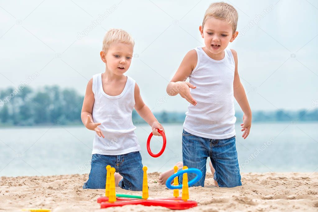 Two brothers are walking and playing on the beach.The game is a ring toss.