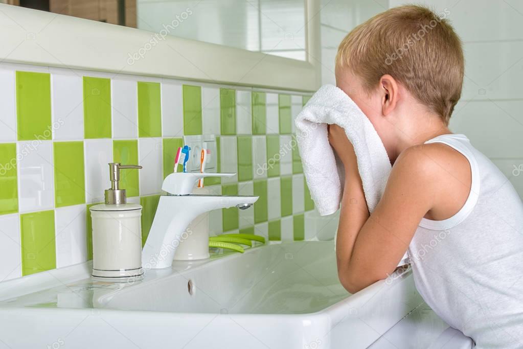 Un niño lava la cara, limpia su rostro con una toalla en el baño — Foto