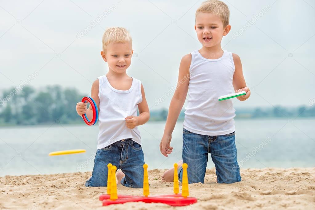  Two brothers are walking and playing on the beach.The game is a ring toss.