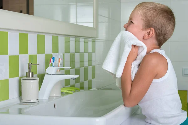 Um rapaz lava o rosto, limpa-lhe o rosto com uma toalha na casa de banho . — Fotografia de Stock