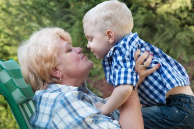 Kucağında oturan küçük torunu kucaklama büyük annesi. Nazik öper. Aile tatili açık havada.