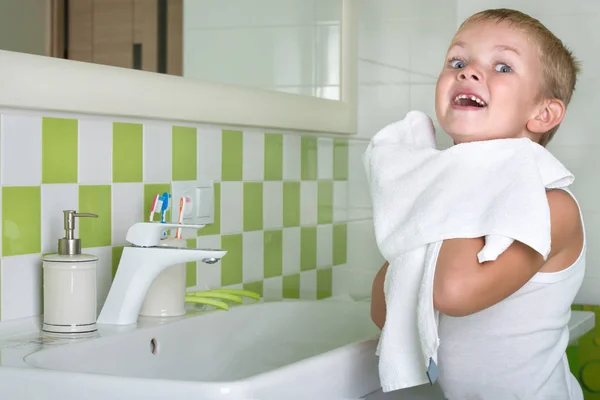 Um rapaz lava o rosto, limpa-lhe o rosto com uma toalha na casa de banho . — Fotografia de Stock
