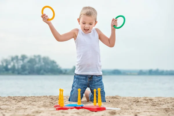 Lindo chico jugando un juego lanzando anillos en el paseo marítimo.La alegría de la victoria . — Foto de Stock