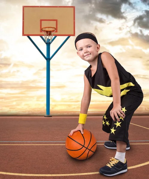 The boy plays basketball on the street.