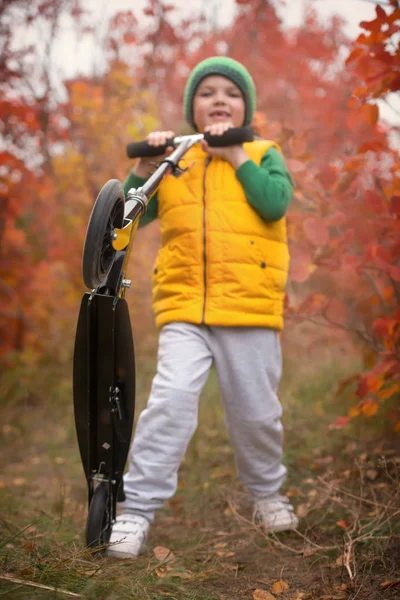 Un niño monta un scooter en el parque de otoño . — Foto de Stock