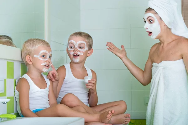 Mutter und Kinder basteln morgens eine Gesichtsmaske. Die Jungs scherzen mit Mama. Schönheitsbehandlungen für die Haut — Stockfoto