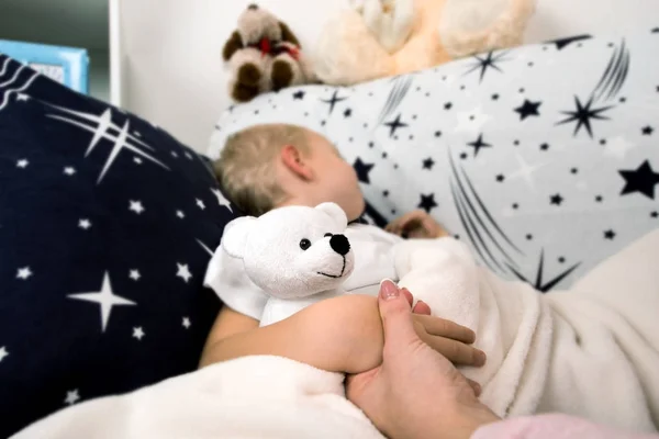 Un niño se acuesta en la cama.Mamá lo besa suavemente antes de dormir. — Foto de Stock