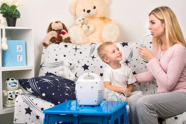 Mujer joven con hijo haciendo inhalación con un nebulizador en casa. Madre de un niño pequeño haciendo inhalación — Foto de Stock