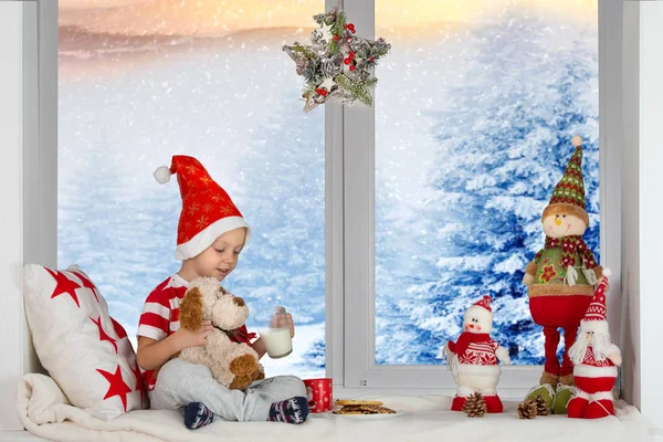 Kellemes karácsonyi ünnepeket és boldog ünnepek! Egy kis fiú ül és játszik egy játékszer kutya eszik a tej és a cookie-k. — Stock Fotó
