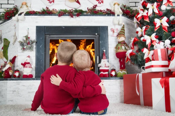 Kellemes karácsonyi ünnepeket és boldog ünnepek! Két testvér, a nappali és a tűz a kandallóban pillantást a padlón ül. A felkészülés a karácsonyi csodák. — Stock Fotó