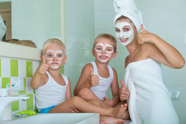 Mutter und Kinder basteln morgens eine Gesichtsmaske. Die Jungs scherzen mit Mama. Schönheitsbehandlungen für die Haut — Stockfoto