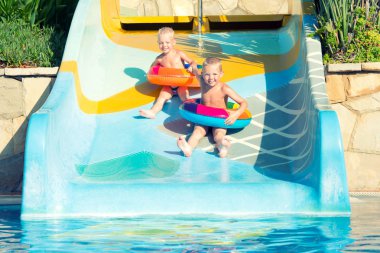 İki kardeş bir şişme lastik çevrelerde el ele tutuşup su taşımak için slayt.