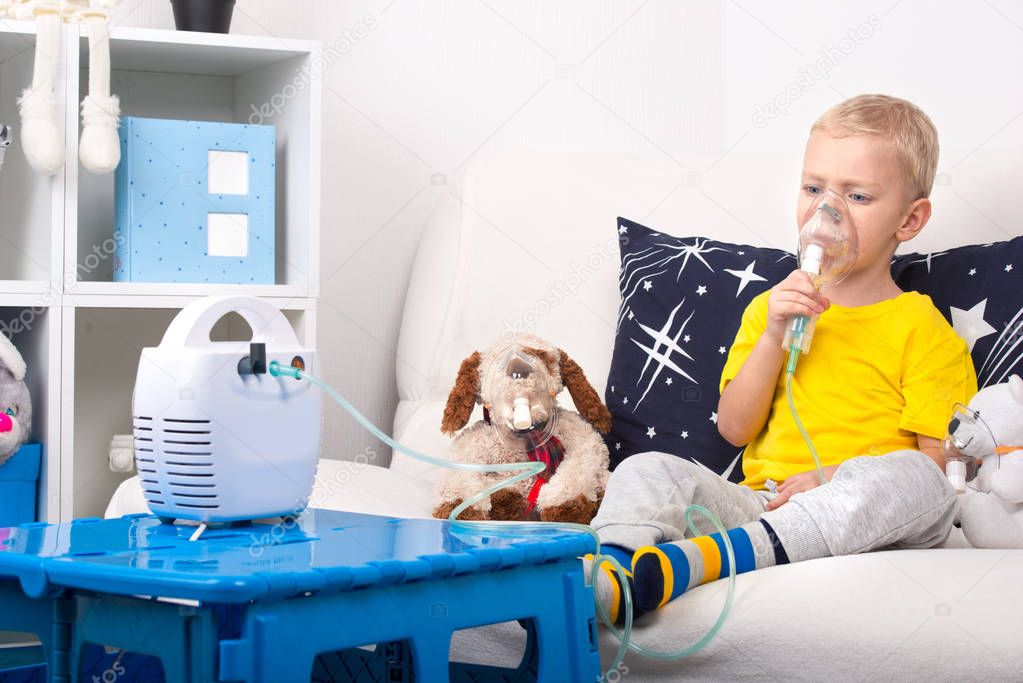 A little boy does inhalation with a nebulizer. A home treatment. A child and a toy dog in masks