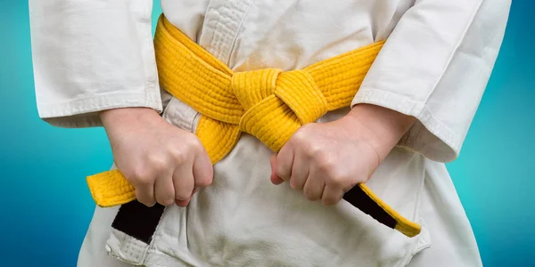 Hands tightening yellow belt on a teenage dressed in kimono for martial arts