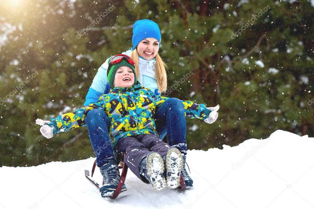 Mother and son ride on sleigh .Child play in snowy forest. Outdoor winter fun for family Christmas vacation.