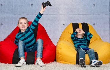 Çocuklar koltuklara oturur ve video oyunları oynarlar. Çocukların duyguları..