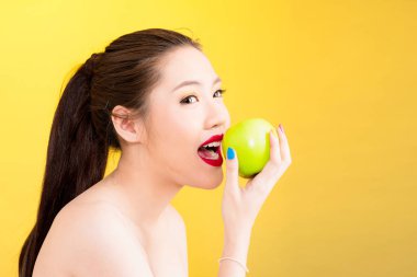 Genç Asyalı kadın sarı arka planda izole elma ısırma