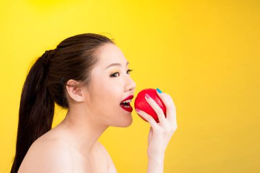 Genç Asyalı kadın sarı arka planda izole elma ısırma