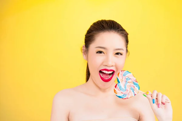 Young Asian woman biting lollipop isolated on yellow background. — Stock Photo, Image