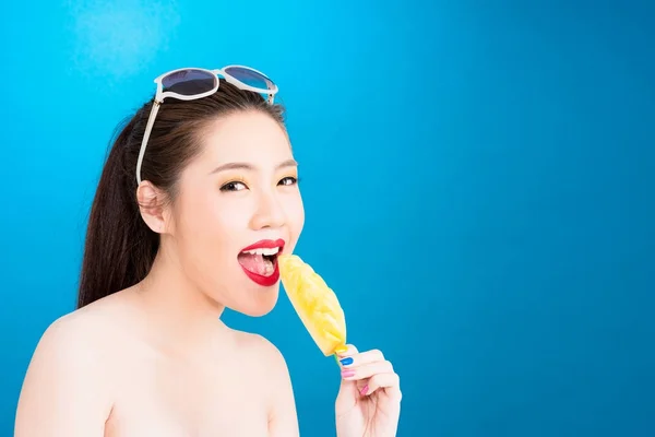 Young Asian woman biting pineapple stick isolated on blue backgr