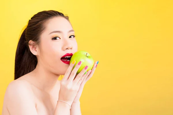 Young Asian woman biting apple isolated in yellow background