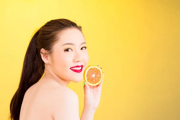 Giovane donna asiatica in possesso di arancione isolato in sfondo giallo . — Foto Stock