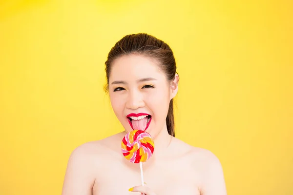 Jovem mulher asiática lambendo pirulito isolado no fundo amarelo — Fotografia de Stock