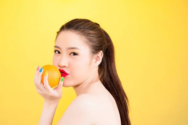 Giovane donna asiatica baciare arancio isolato in fondo giallo . — Foto Stock