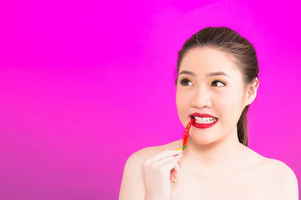 Young Asian woman biting chili isolated in pink background. — Stock Photo, Image