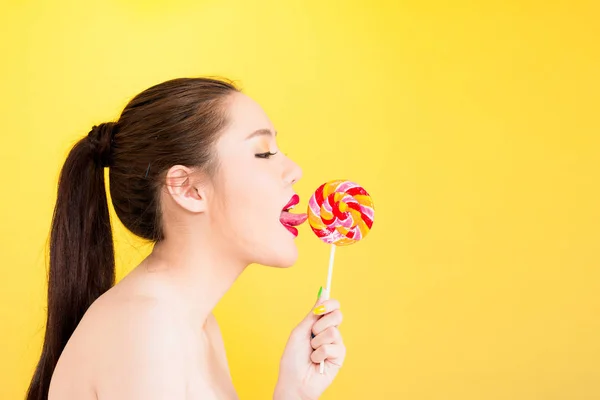 Young Asian woman licking lollipop isolated on yellow background — Stock Photo, Image