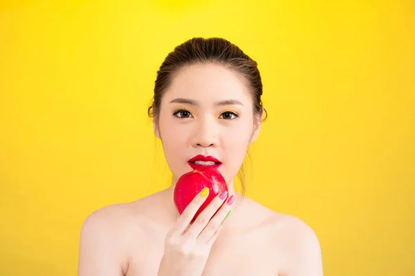Молодая азиатка ест яблоко на желтом фоне — стоковое фото
