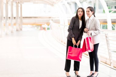 Birlikte alışveriş iki güzel kız. Asyalı kadın ve beyaz kız akıllıca iş gün içinde öğle yemeği saatinde alışveriş elbise. İş bölgesi yürüyüş ile doğal ışıklar açık alınan yol.