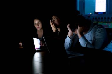 Fazla mesai konsepti. Bir grup genç iş adamı, görevlerini tamamlamak için gece geç saatlere kadar toplantı odasında çalışıyorlar. Arka planda ofis binası ile modern ofiste çekilmiş..