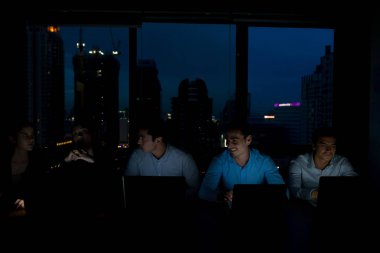 Işıkları ve bilgisayar dizüstü ekran ışığı ile gece geç saatlerde bir motivasyonu yüksek iş ekibi. İçeren 5 genç insanlar, 2 kadın, 3 erkek güzel Asyalı kadınla ve yakışıklı beyaz adam.