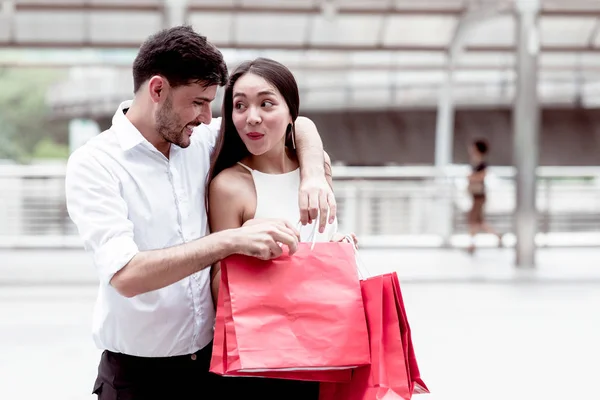 Happy couple talking after a hard day of huge sale shopping in asian country. Young handsome white male and beautiful asian female with red shopping bag looking very satisfy. Apply urban looks.