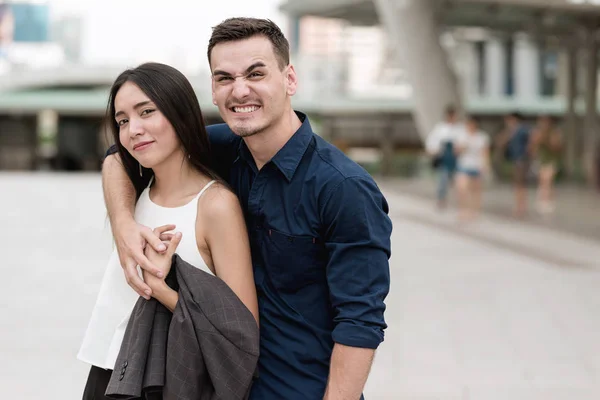Happy young  interracial couple. Happy Handsome young white male holding a young beautiful asian female very tight with a smile in public place showing his love to his future wife. Apply urban looks.