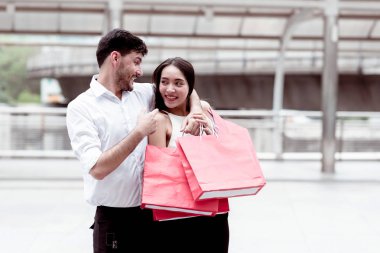 Happy couple talking after a hard day of huge sale shopping in asian country. Young handsome white male and beautiful asian female with red shopping bag looking very satisfy. Apply urban looks. clipart