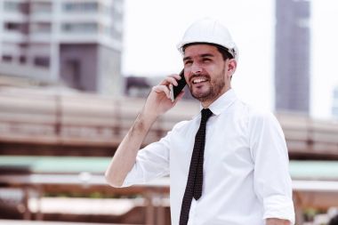 Mobil ofis kavramı. Finansal arka planda bina ile cep telefonu patronuyla konuşurken yakışıklı beyaz erkek mühendis. Açık ele alındığında, kentsel görünüyor efekti uygula.