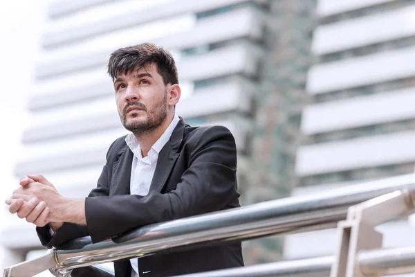 Sad and stress out handsome stressful white business man or sale man looking up day dreaming with financial building in background. Taken outdoor, apply urban looks effect.